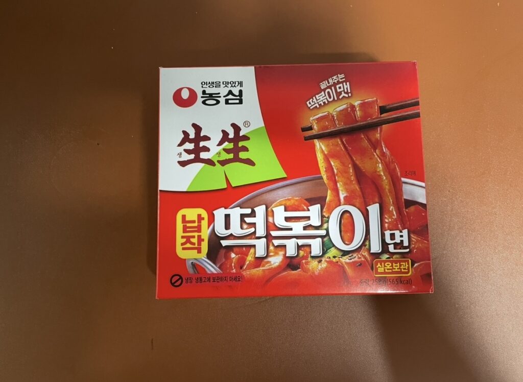  Front of the product box — (napjak tteokbokki ramen)
Front of the napjak tteokbokki ramen box in a red package, with an image of chopsticks holding the flat noodles and spicy sauce.