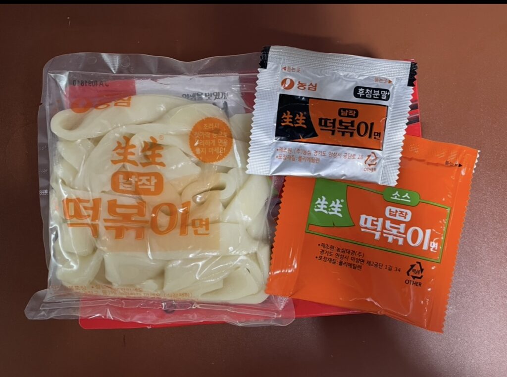 Flat rice cakes in a clear pouch, with sauce and seasoning packets placed together, helping people searching Where to buy Korean snack understand what’s inside the product