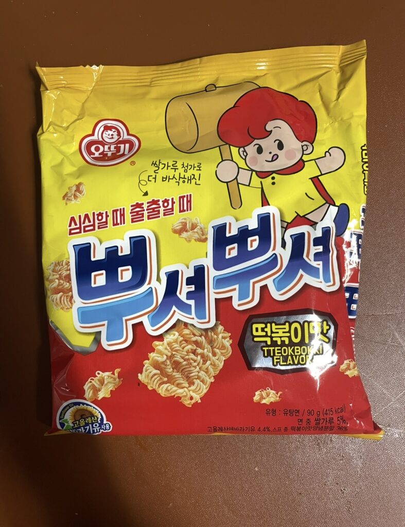 A front view of the Ppushuppushu Tteokbokki package with a cute character on a yellow background. It’s a signature image of a sweet and spicy Korean ramen snack