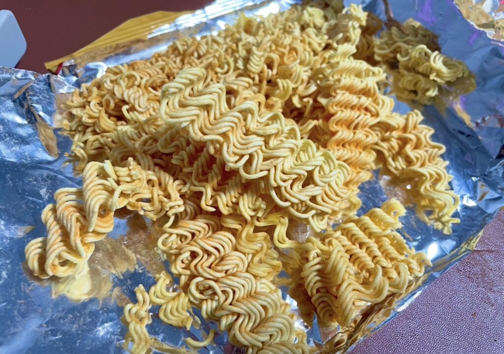 A photo of the noodles after mixing with the seasoning powder. The color highlights the blend of gochujang aroma and sweetness typical of Korean snack flavors