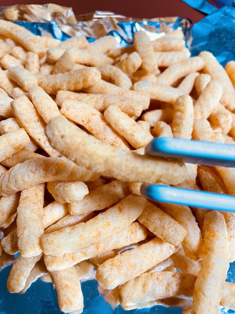 close-up shot of a single maewoon saewookkang piece held with tongs, showing crispy texture for detailed korean snack review visuals