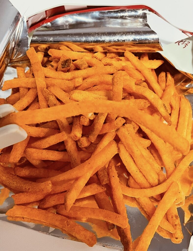 A close-up shot of a hand holding one piece of Nuneul Gamja Chili Cheese Fries Flavor.
The red seasoning evenly covers the surface, vividly conveying the heat and crunch typical of Spicy Korean snack flavors