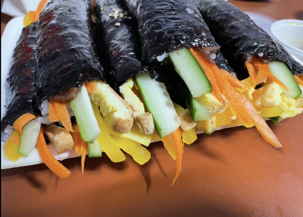 an overhead shot of the opened package showing multiple small rolls arranged neatly, capturing the tidy and glossy appearance of bite-sized kimbap