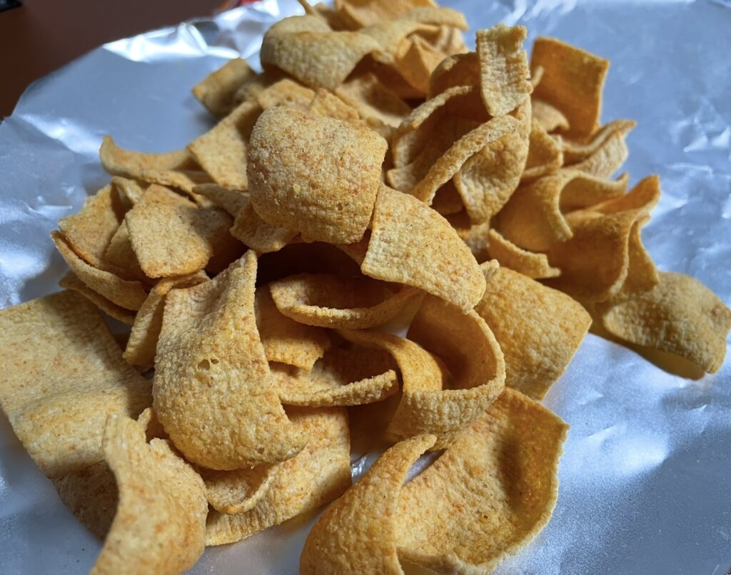 Chips taken out of the bag and spread on a surface, visually highlighting the chili-salsa seasoning and representing typical korean snack flavors.