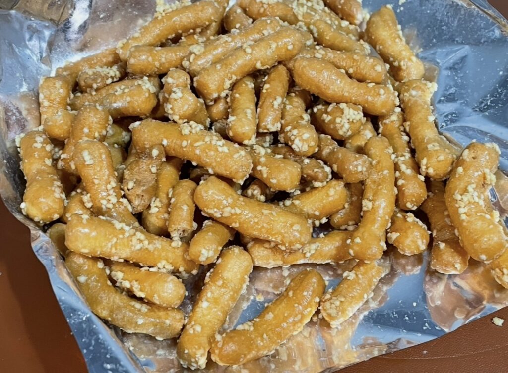 golden brown fried snacks poured onto a white plate, coated with sweet syrup and peanut pieces that create unique korean snack flavors.
