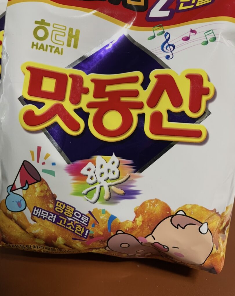a front view of the bright red and yellow package of matdongsan, featuring a cheerful cartoon character and korean text.